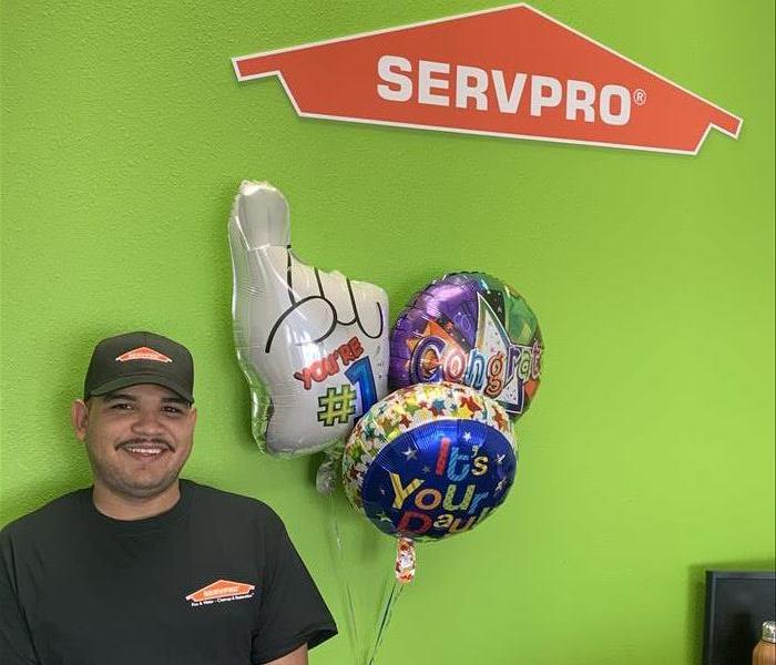 Photo is showing a restoration technician wearing a SERVPRO uniform, standing near balloons