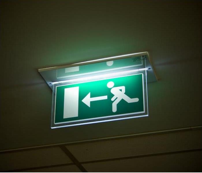 Photo is a green sign showing an arrow and a door that leads to the exit in case of an emergency