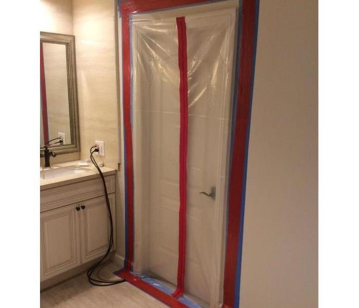 Clear plastic taped in front of a doorway with a zipper down the middle to provide access in and out of affected area.