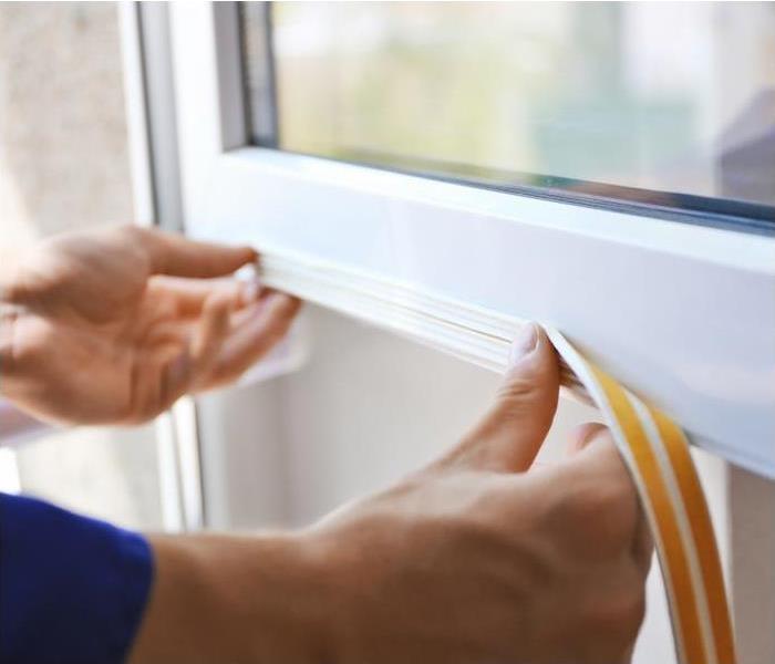Photo is showing a person applying weather strips to a window to seal it from harsh weather. 
