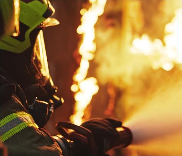 Photo is showing a firefighter fighting a fire by spraying the fire with a water hose