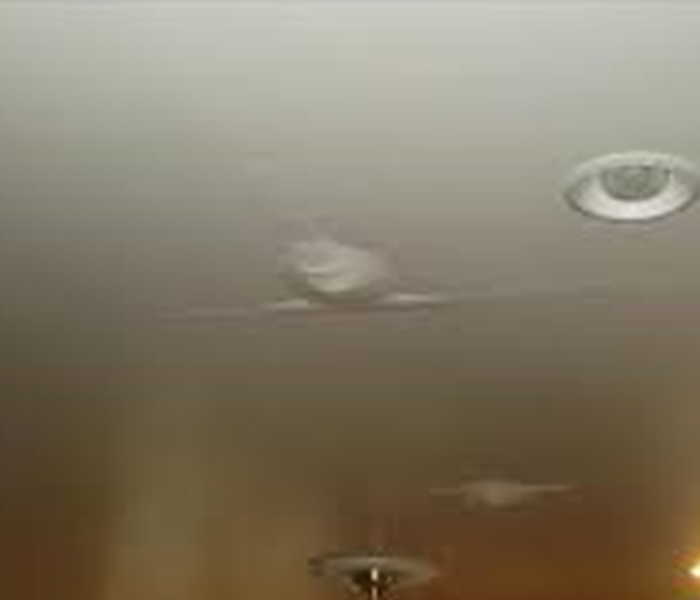 Photo is showing a ceiling that has water damage. The paint is sagging and filled with water. 