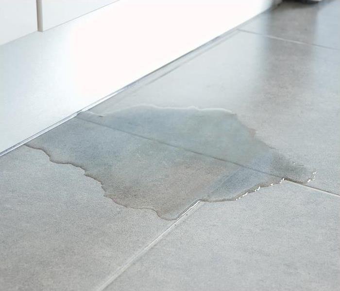 Water seeping out onto a tile floor from underneath a baseboard
